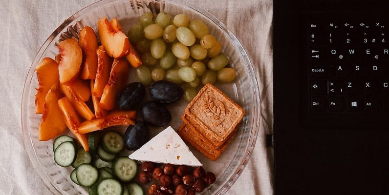 A delightful snack plate with fruits, cheese, and a laptop for a healthy lifestyle.
